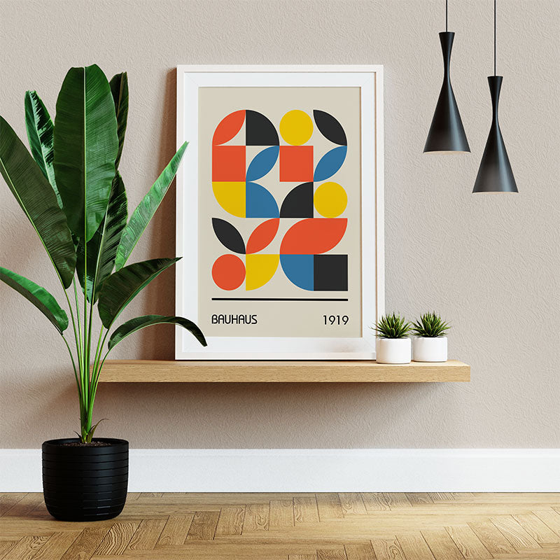 Quadro Decorativo Geométrico Bauhaus com moldura branca apoiado em prateleira, ao lado de plantas e luminárias pretas.