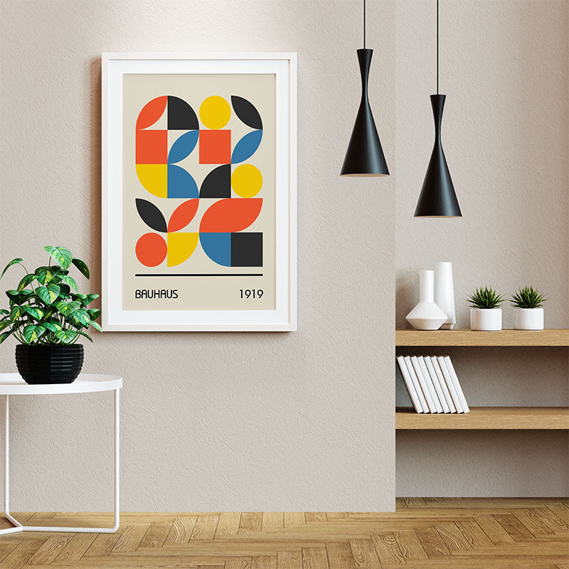 Quadro Decorativo Geométrico Bauhaus com moldura branca pendurado em parede bege, ao lado de luminárias pretas e prateleira decorada.