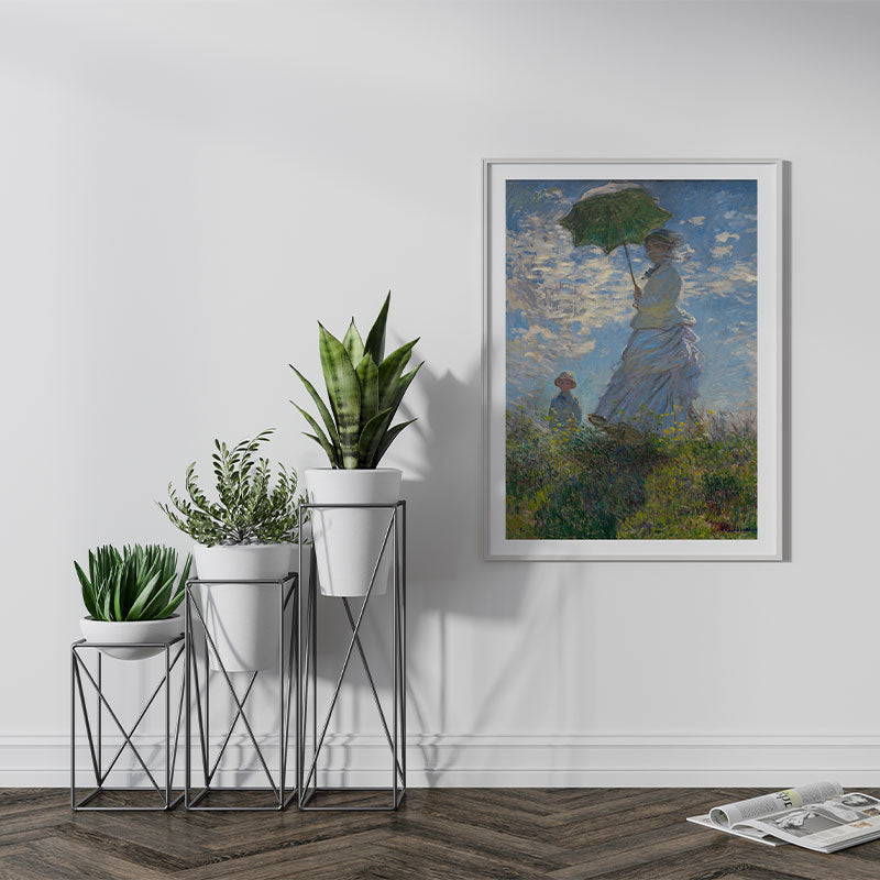 Quadro Decorativo Mulher com Sombrinha Pendurado ao Lado de Planta Verde.